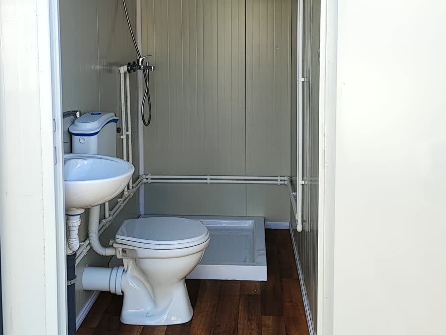Innenansicht eines Sanitärcontainers mit Waschbecken, WC, Duschtasse und Aufputz-Leitungen